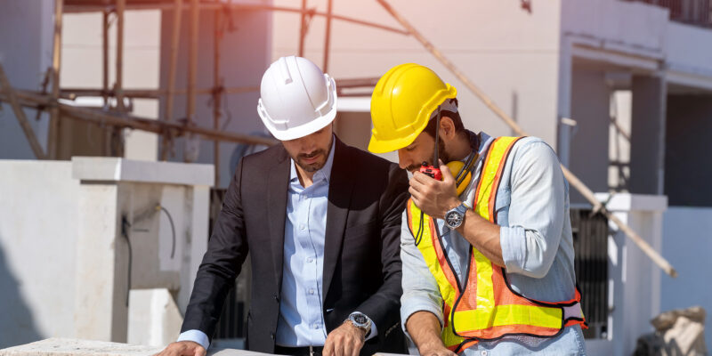 Projektleitung Zwei Männer unterhalten sich auf der Baustelle. Vor ihnen liegt ein Bauplan.
